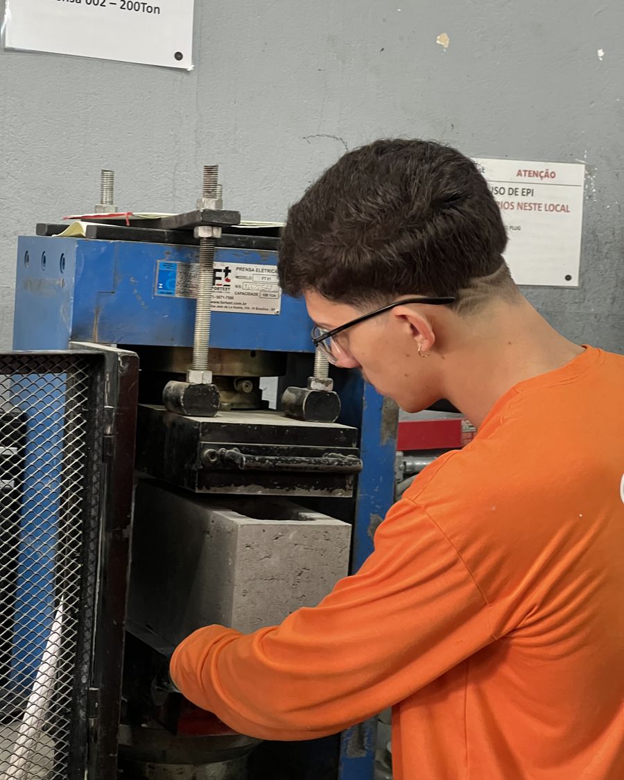Técnico posicionando bloco de concreto na prensa para ensaio de compressão